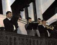Three members of the trombone choir play in the left balcony while others play in the balcony opposite them.