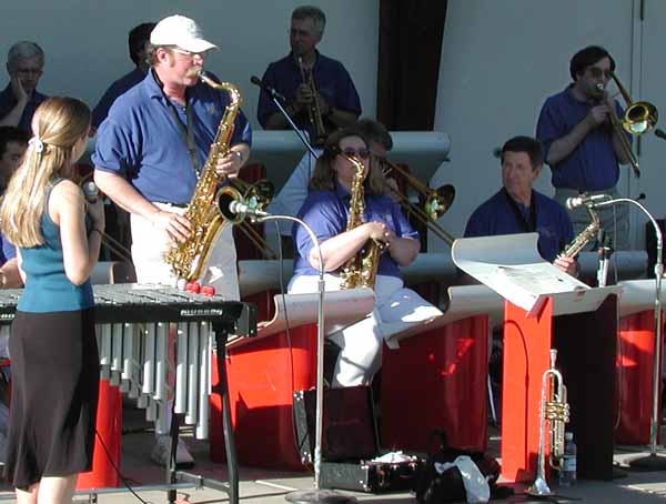 Glen Peterson plays tenor sax and Rich Eyman plays trombone as vocalist Sarah Morris and band members look on.