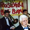 Part of the trombone section plays in front of the Roseville Big Band sign.