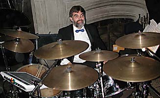 Jim is surrounded by cymbals, toms, and other drum equipment. 