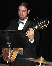 Nick, with tux, blue tie and cummerbund, plays a guitar solo.