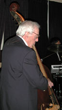 Ted plucks the upright bass while wearing a suit.